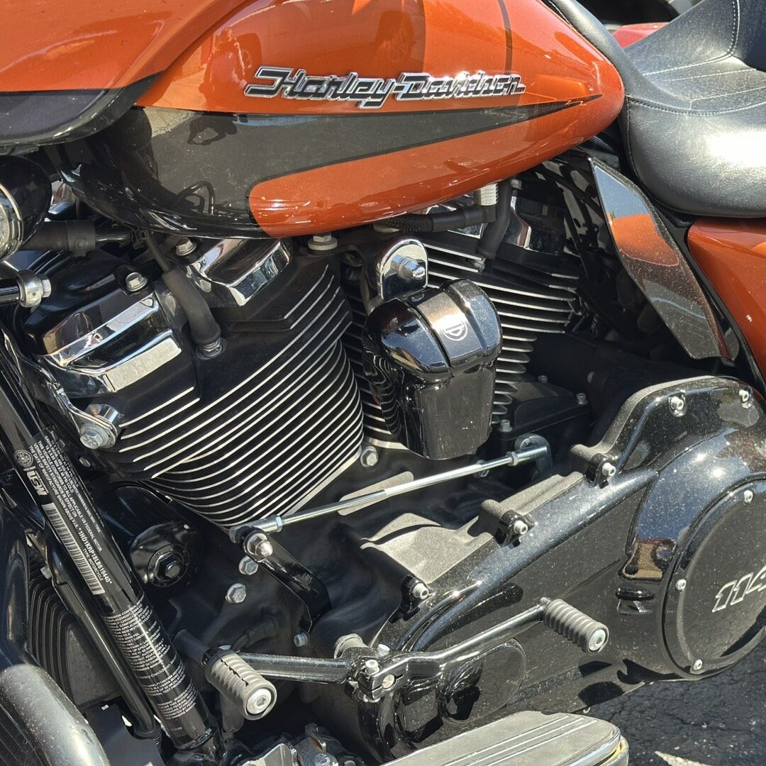 Orange Harley-Davidson motorcycle with a visible chrome V-twin engine and black frame, close-up of the midsection and seat area.